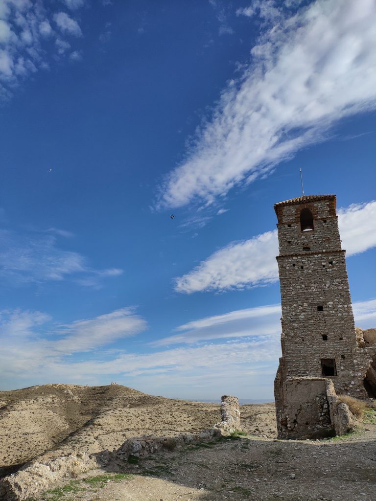 Torre de la iglesia del pueblo viejo de Rodén sobre un paisaje árido, bajo un cielo despejado con nubes dispersas.