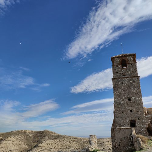 Torre de la iglesia del pueblo viejo de Rodén sobre un paisaje árido, bajo un cielo despejado con nubes dispersas.